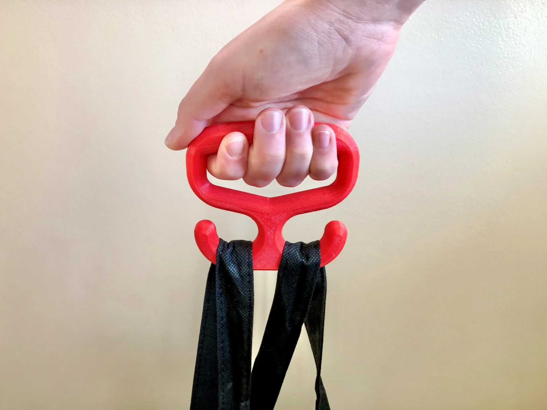A hand holding a red 3D printed bag carrier with a black bag on its hooks