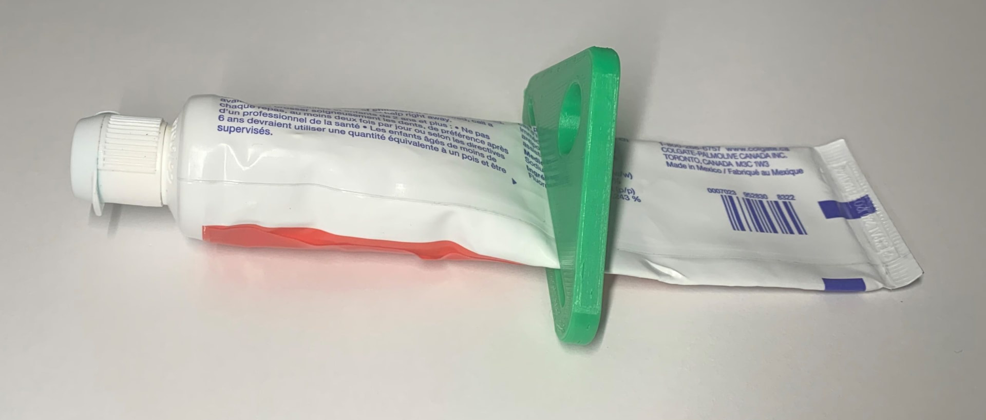 A green 3D printed toothpaste squeezer sitting on a toothpaste tube, showing how the tube is pulled through the slot