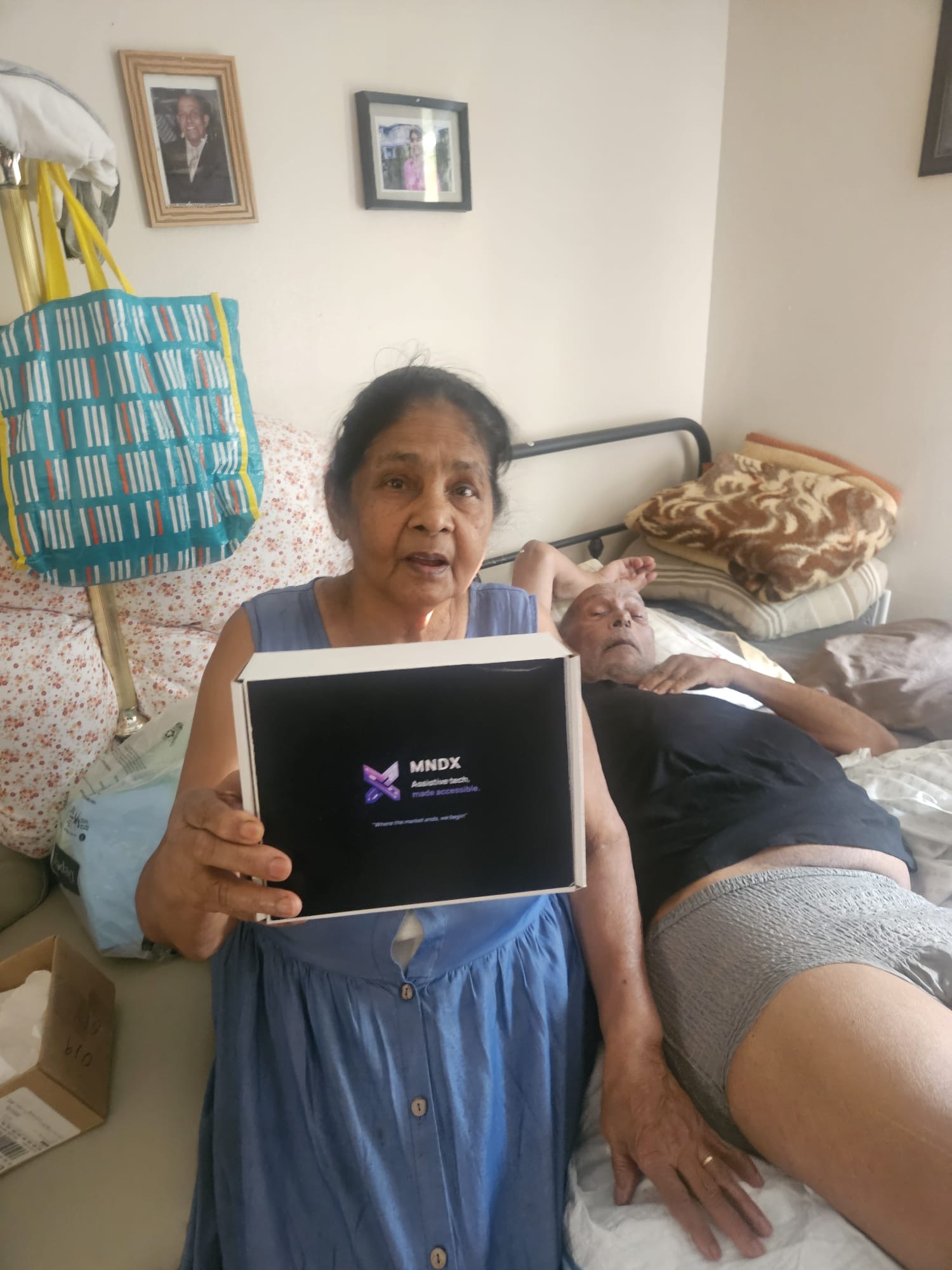 A woman holding an MNDX device box beside a family member resting in bed